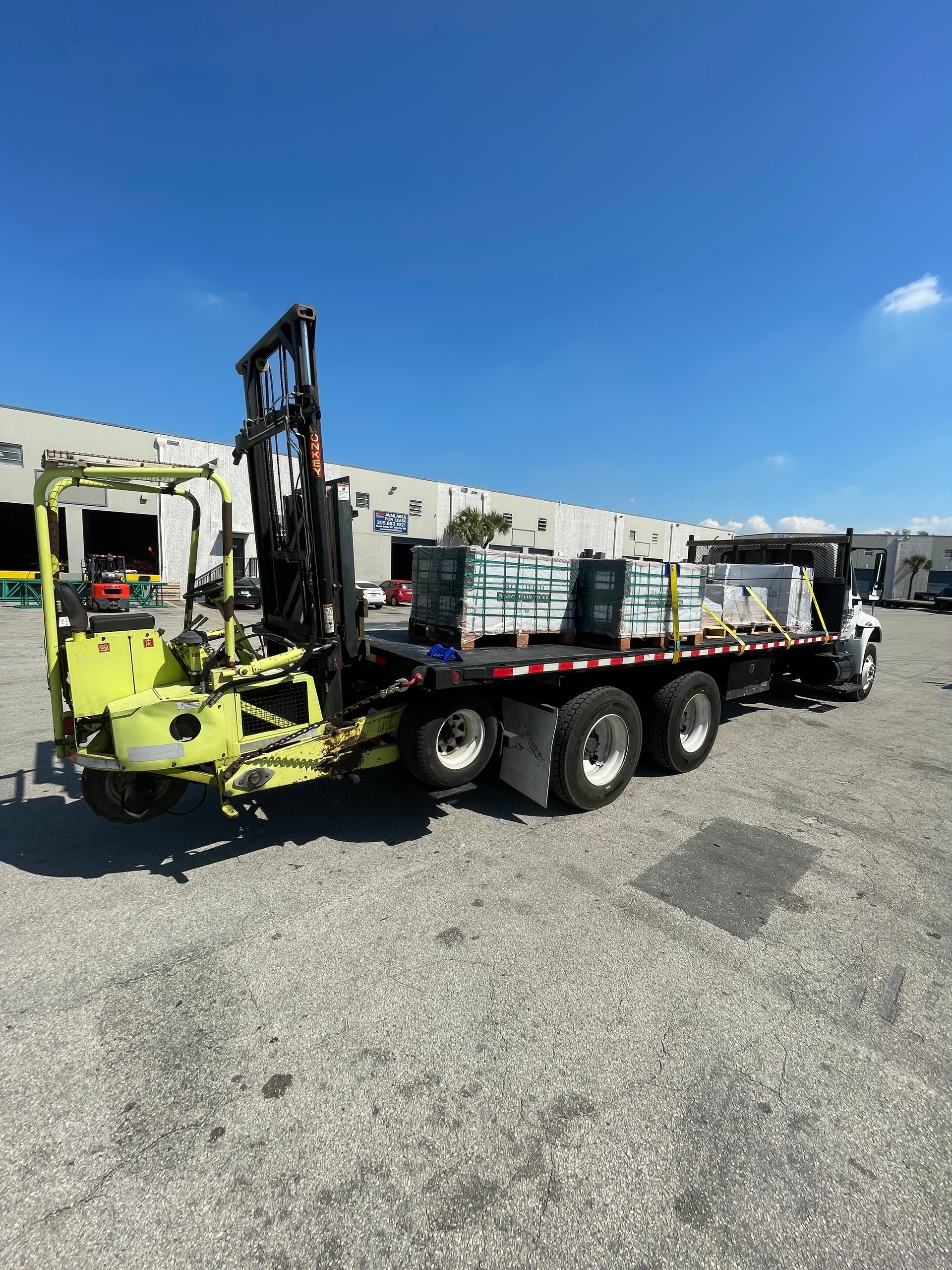 Yellow and black industrial flatbed truck with mounted forklift on asphalt lot under clear blue sky