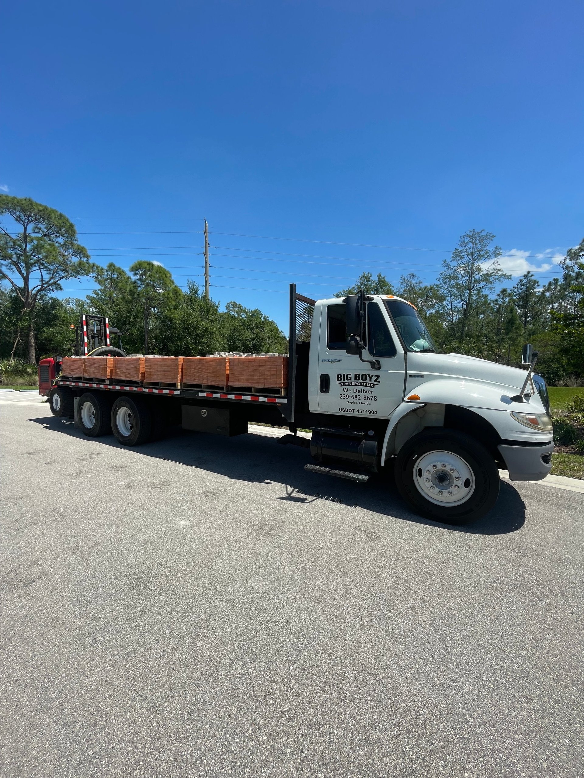 White flatbed truck with Big Boyz branding parked on asphalt road with trees in background under clear blue sky
