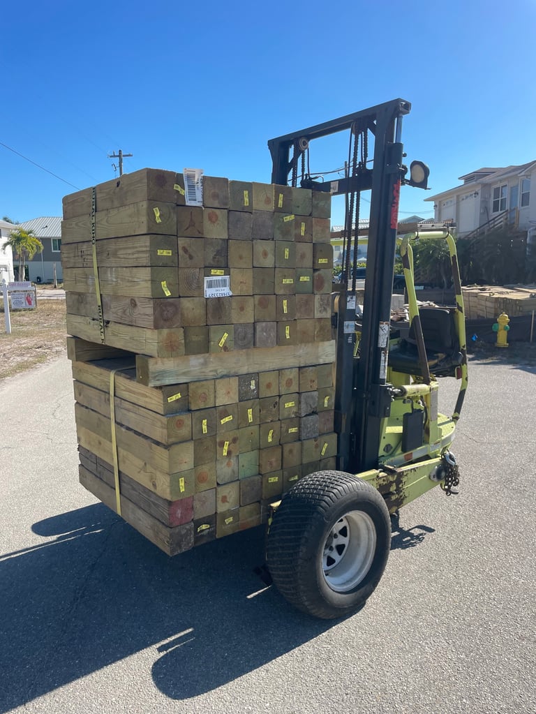 Yellow forklift loaded with large stack of wooden shipping crates in a parking lot on a sunny day
